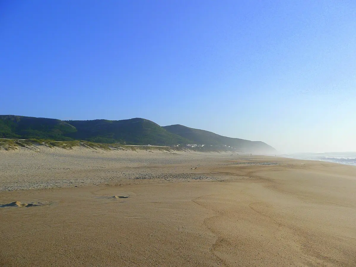 Praia de areia extensa em Quiaios, com serra verde ao fundo e céu limpo