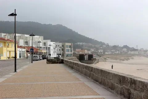 Passeio marítimo pavimentado junto à praia de Moledo, com casas e monte ao fundo em dia de nevoeiro