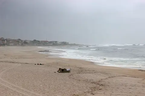 Praia extensa de areia em Moledo com ondas e casario ao fundo em dia nublado
