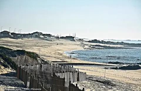 Praia de Labruge com paliçadas de madeira nas dunas, areal extenso e rochas junto ao mar