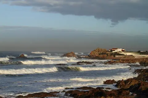 Costa rochosa da Boa Nova com ondas a rebentar e capela branca sobre as rochas ao fundo