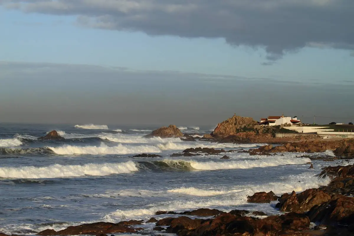 Costa rochosa da Boa Nova com ondas a rebentar e capela branca sobre as rochas ao fundo