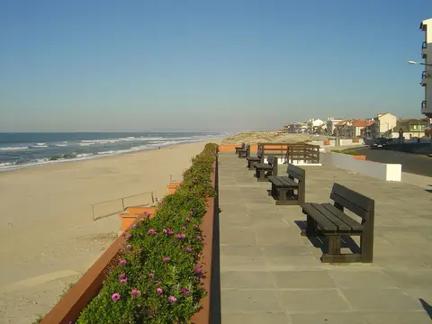 Passeio marítimo com bancos de madeira e flores junto ao areal da praia de Pedrógão