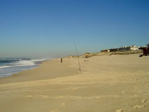 Praia de Pedrógão com areal extenso, pescador ao longe e casas junto às dunas