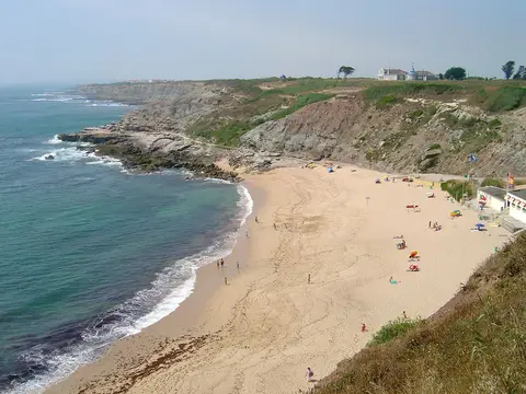 Praia de areia de S. Bernardino vista do alto, com falésias, mar azul e banhistas ao longe