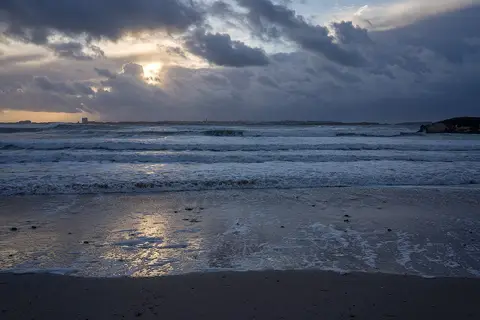 Praia do Baleal ao pôr do sol, com ondas a rebentar e céu nublado sobre o areal molhado