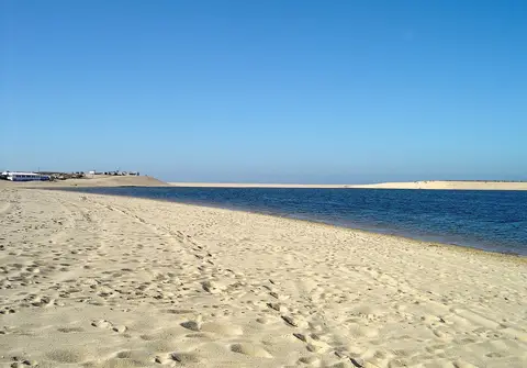 Praia de areia junto à água calma da Lagoa de Albufeira, com céu azul limpo