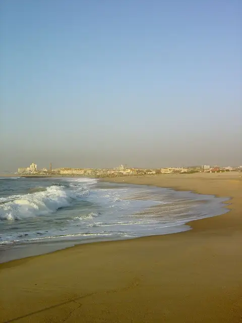 Praia de areia em Silvalde com ondas a rebentar e a povoação ao fundo, ao entardecer
