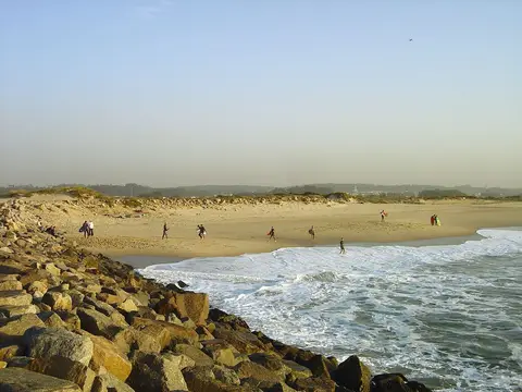 Praia de Silvalde com areal extenso, ondas e molhe de rochas em primeiro plano
