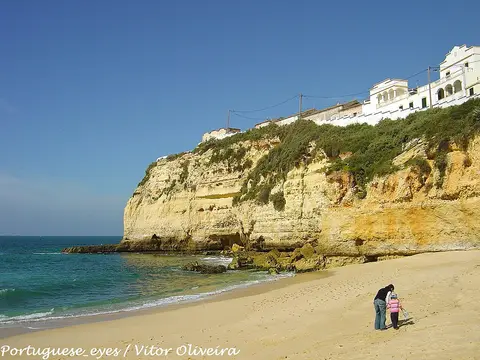 Praia de areia do Carvoeiro com falésias douradas, mar azul e casas brancas no topo da arriba