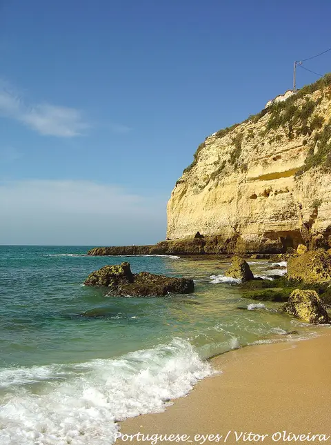 Praia do Carvoeiro com falésia dourada, rochas e ondas sobre a areia, no Algarve