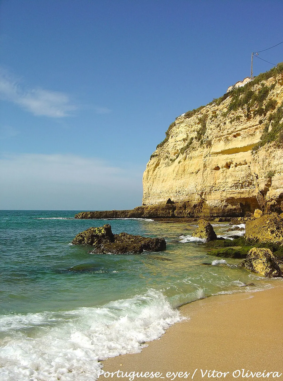 Praia do Carvoeiro com falésia dourada, rochas e ondas sobre a areia, no Algarve