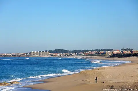 Praia do Aterro com areal extenso, ondas e casario ao fundo sob céu azul