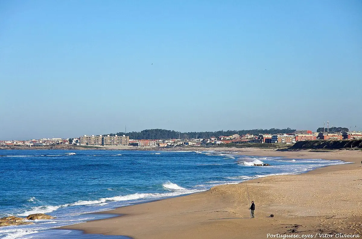 Praia do Aterro com areal extenso, ondas e casario ao fundo sob céu azul