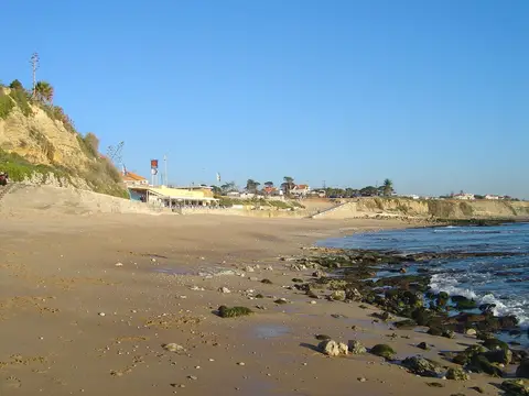 Praia de S. Pedro do Estoril com areia, rochas cobertas de algas e falésia ao fundo