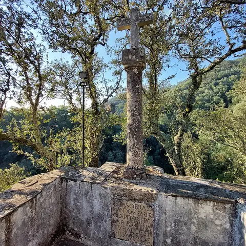Cruzeiro de pedra com inscrição no santuário da Senhora da Piedade, na Lousã, rodeado de árvores