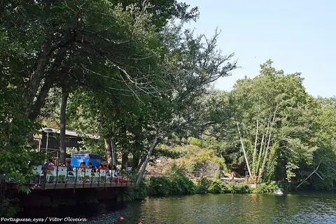 Praia fluvial da Bogueira com esplanada de madeira junto ao rio, rodeada de árvores