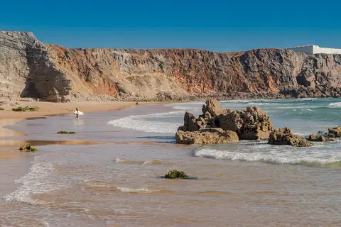 Praia do Tonel com falésias, rochas na rebentação e um surfista ao longe na areia