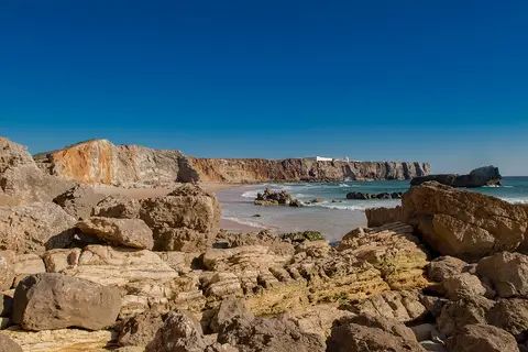 Praia do Tonel com rochas em primeiro plano, falésias douradas e mar azul sob céu limpo
