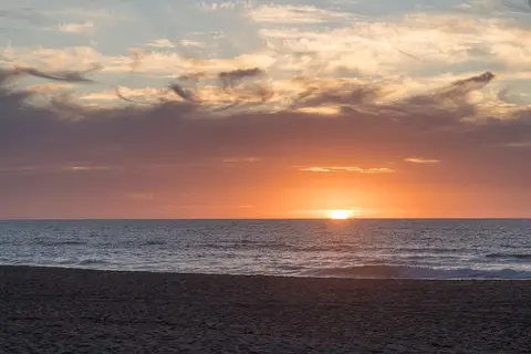 Pôr do sol sobre o mar na praia da Foz do Sizandro, com areia em primeiro plano