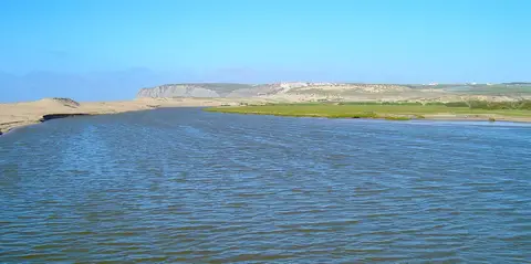 Foz do rio Sizandro, com areal, vegetação e falésias ao fundo sob céu azul