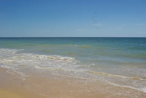 Areal e mar calmo na praia da Oura, em Albufeira, sob céu azul limpo