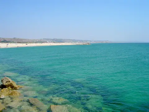 Praia de areia junto a água turquesa na Cova do Vapor, com rochas em primeiro plano