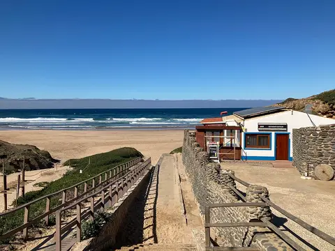 Entrada da Praia do Castelejo com escadaria, restaurante e areal junto ao mar.