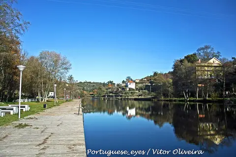 Praia fluvial de Ponte de Juncais com passadiço de madeira junto ao rio e casas ao fundo