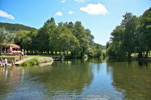 Praia fluvial das Canaveias, com rio calmo rodeado de árvores e zona relvada com esplanada