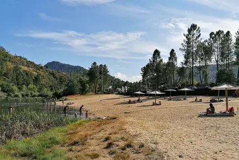 Praia fluvial de Janeiro de Baixo com areal, chapéus de sol e rio rodeado de encostas arborizadas