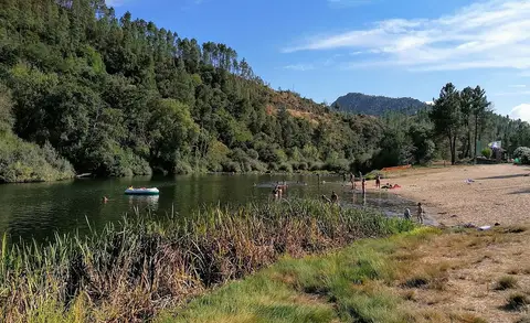 Praia fluvial de Janeiro de Baixo, com areal junto ao rio e encostas arborizadas ao fundo