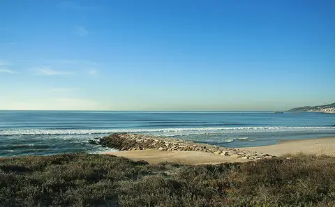 Praia da Cova-Gala com esporão de rochas, dunas com vegetação e mar calmo sob céu azul