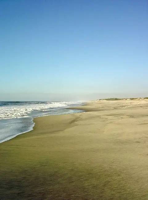Praia deserta de areia larga com ondas a rebentar e céu azul limpo, no Torrão do Lameiro