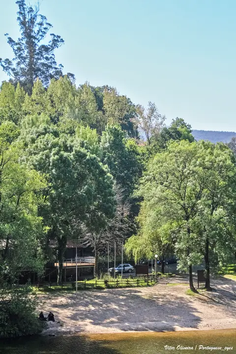 Praia fluvial da Quinta do Barco, com areal junto ao rio rodeado de árvores e apoio de madeira