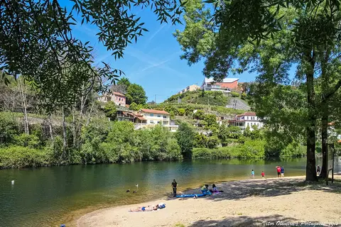 Praia fluvial da Quinta do Barco, com areal, rio e casas na encosta arborizada