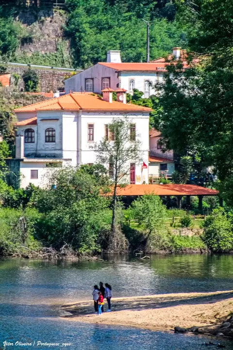 Praia fluvial junto à Quinta do Barco, com casas de telhado vermelho e vegetação sobre o rio