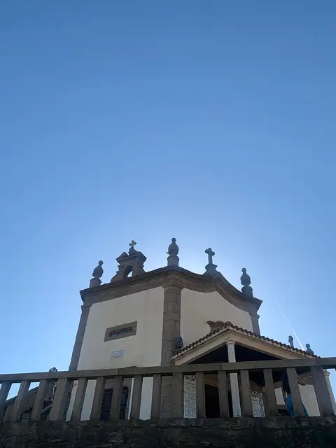 Capela do Senhor da Pedra vista de baixo, com balaustrada de pedra e céu azul limpo