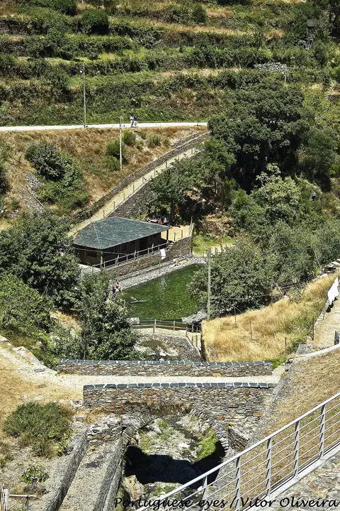 Vista aérea da praia fluvial do Piódão, com piscina, edifício de xisto e encostas verdes em socalcos