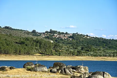 Albufeira de Vilar com rochas graníticas na margem e aldeia na encosta arborizada ao fundo