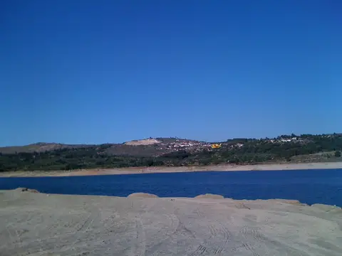 Albufeira do Vilar com margem de areia em primeiro plano e aldeia na encosta ao fundo