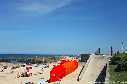Praia de Leça da Palmeira com barracas vermelhas, rochas e farol ao fundo