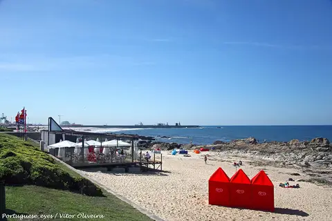 Praia de Leça da Palmeira com areal, rochas, bar de praia com guarda-sóis e cabinas vermelhas