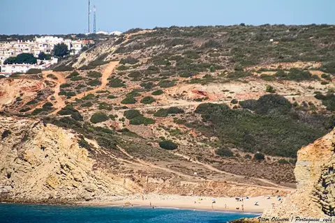 Praia da Boca do Rio vista de longe, com falésias, vegetação e banhistas na areia junto ao mar
