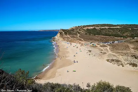Vista panorâmica da Praia da Boca do Rio, com areal extenso, mar azul e falésias.