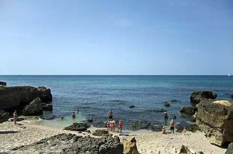Pequena enseada da Praia do Evaristo com rochas, areia e mar azul, com banhistas ao longe