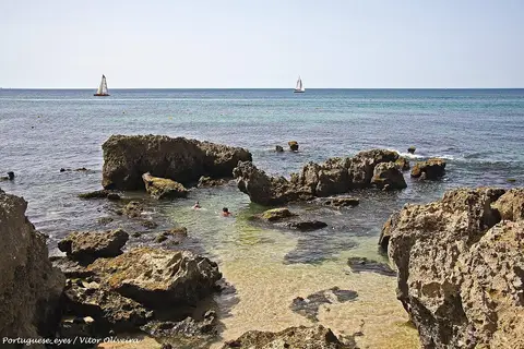 Praia do Evaristo com formações rochosas, água transparente e veleiros ao largo