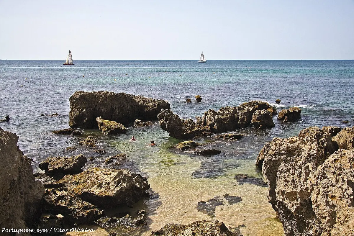 Praia do Evaristo com formações rochosas, água transparente e veleiros ao largo