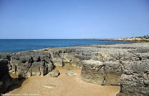 Formações rochosas e areia na Praia do Evaristo, com mar azul e costa ao fundo