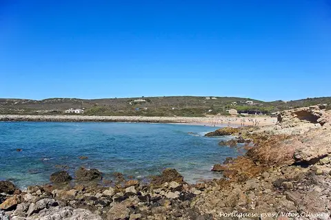 Praia da Ingrina vista das rochas, com mar azul e banhistas ao longe no areal